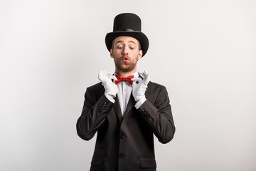 Wall Mural - emotional magician adjusting red bow tie, isolated on grey