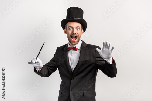 Cuadros en Lienzo excited magician in suit and hat holding wand, isolated on grey
