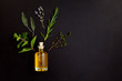 Essential oil of herbs for spa treatments. Bottle of natural oil with ingredients on black background, top view