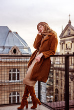 Outdoor Full-length Portrait Of Elegant Fashionable Woman Wearing Trendy Monochrome Beige, Brown Outfit: Beret, Dress, Faux Fur Coat, High Suede Over Knee Boots, Posing In European City