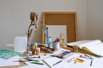 Interior of painting studio of freelance artist. Gypsum shapes, brushes, pencills, ink and paint bottles with sketchbooks on the table. Freelance artist lifestyle concept. Copy space