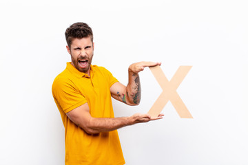 young handsome man angry, anger, disagreement, holding the letter X of the alphabet to form a word or a sentence.