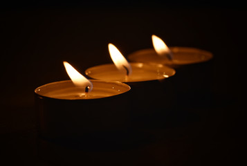 A row of three small candles in aluminum candlesticks on a black background