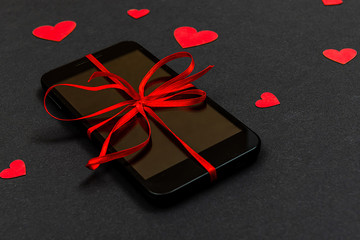 Valentine day, Christmas gift concept, on dark background isolated red paper hearts and smartphone with red ribbon