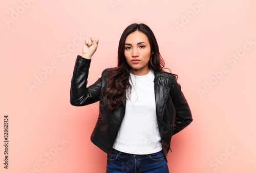 Fotomural young latin pretty woman feeling serious, strong and rebellious, raising fist up