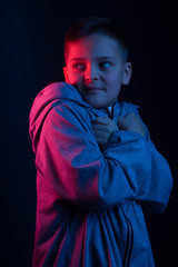 Studio portrait of a dark-haired boy, on a dark background, in a hoodie jacket.