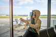 © PHILIPPE DEGROOTE/ADDICTIVE STOCK - Preteen boy in hooded outwear and VR goggles gesturing and exploring virtual reality while sitting near window in modern airport