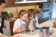 © PHILIPPE DEGROOTE/ADDICTIVE STOCK - Stock photo of children in aprons looking at a container in the kitchen and preparing cupcake