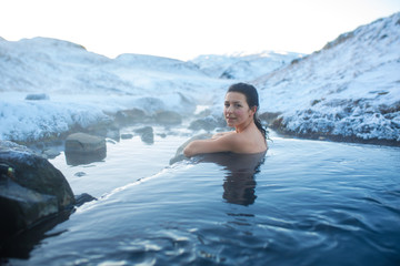 Wall Mural - The girl bathes in a hot spring in the open air with a gorgeous view of the snowy mountains. Incredible iceland in winter