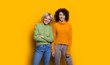 © Strelciuc - Portrait of two happy lovely sisters one with blonde hair another with curly hair looking at camera laughing isolated on yellow studio wall.