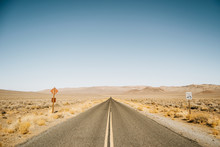Empty Straight Road With Traffic Signs In Desert Of USA On Sunny Day