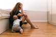 © Полина Власова - A married woman sits on the floor with her crawling baby in the bedroom after a family quarrel, bruises on her body, signs of beatings. Domestic violence, abuse. Black and white