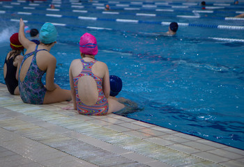 Two little girl sitting side by side on the swimming pool edge.