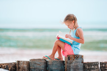 Little adorable girl reading book during tropical white beach