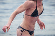 Unknown woman in black bikini getting out of the cold water in winter time, with drops falling from her breasts.