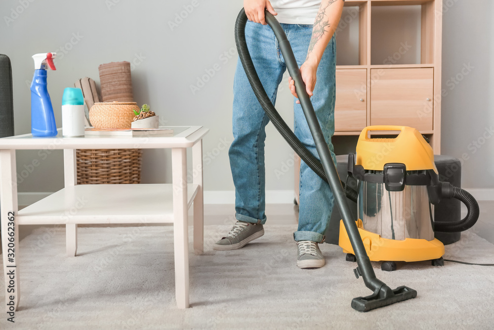 Young Asian man hoovering floor at home