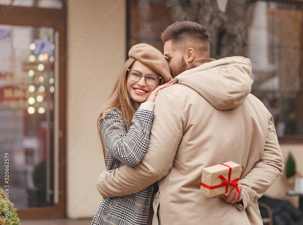 Happy man hiding gift for his girlfriend outdoors