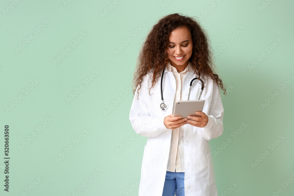 Young African-American doctor with tablet computer on color background