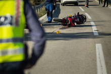 Car And A Red Sport Motorcycle Crash Scene On An Open Road In Afternoon. Workers And Police Seen Around The Crash Site, With A Queue Of Traffic Building Behind. View From Behind The Police Officer.