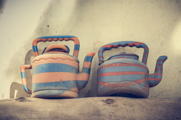 A pair of old and worn kettles for tea or water in a blue and orange color, resting on a wooden board outside.