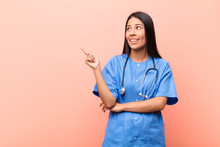 Young Latin Nurse Smiling Happily And Looking Sideways, Wondering, Thinking Or Having An Idea Against Pink Wall