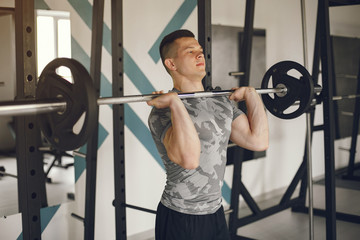 Sports man in the gym. A man performs exercises. Guy in a gray t-shirt