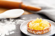 Pineapple tart or tartlet with grated coconut in a small plate on a slate with flour and baking utensils.