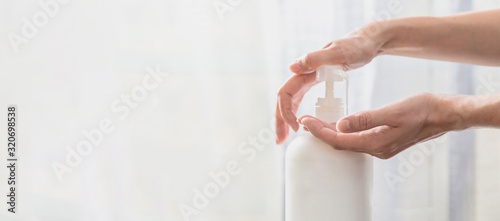 Fotomural Woman hands pushing pump plastic soap bottle on white background with copy space