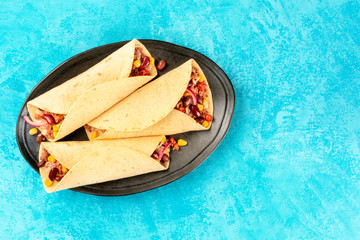 Wall Mural - Burrito sandwich wraps, overhead shot on a blue background. Mexican tortillas with minced beef meat, rice, beans, onions, and chilli peppers, with copyspace