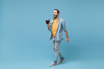 Wall Mural - Cheerful traveler tourist man in yellow summer casual clothes with photo camera on neck isolated on blue background. Male passenger traveling abroad on weekends getaway. Air flight journey concept.