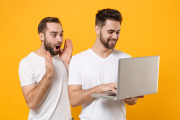 Wall Mural - Amazed young men guys friends in white blank t-shirts posing isolated on yellow orange wall background studio portrait. People lifestyle concept. Mock up copy space. Working on laptop pc computer.