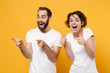 © ViDi Studio - Excited young couple friends bearded guy girl in white t-shirts posing isolated on yellow orange background. People lifestyle concept. Mock up copy space. Point index fingers aside, showing thumbs up.