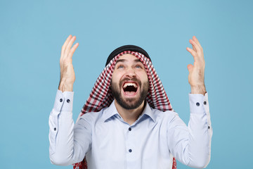 Crazy bearded arabian muslim man in keffiyeh kafiya ring igal agal casual clothes isolated on pastel blue background. People religious lifestyle concept. Mock up copy space. Screaming spreading hands.