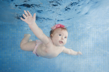 Little baby girl learning to swim underwater in a swimming pool. Healthy family lifestyle and children water sports activity.