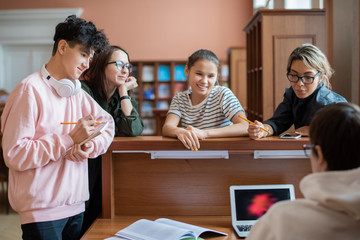 Poster - Group of clever college student standing by programmer in front of laptop helping them to find information for seminar