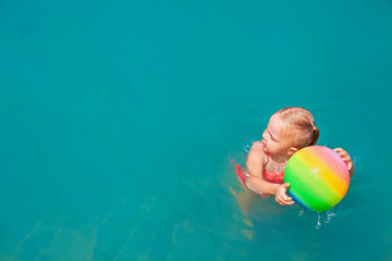 Wall Mural - Active happy child have fun on summer beach holiday. Funny baby girl playing with ball. Aquatic game in swimming pool, top view. Healthy family lifestyle, summer travel with kids on tropical resort.