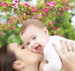 Canvas Print - family and motherhood concept - close up of young mother kissing happy little baby over natural spring cherry blossom background