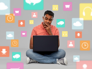 Poster - technology and people concept - thinking indian man with laptop computer sitting on floor over mobile app icons on grey background