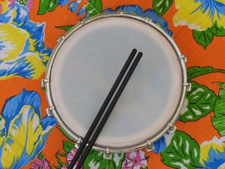 A Brazilian percussion musical instrument: tamborim with drumstick, on a colorful “chitao” fabric with floral prints. It is used to play samba music and has great prominence in the carnival.