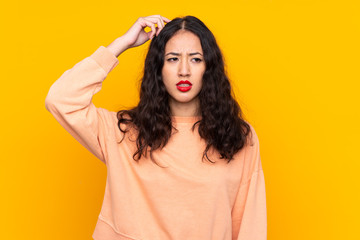 Wall Mural - Spanish Chinese woman over isolated yellow background having doubts while scratching head