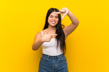 Wall Mural - Young teenager Asian girl over isolated yellow background focusing face. Framing symbol