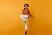 Full-length Photo Of Elegant European Female Model Dancing With Excitement. Studio Shot Of Slim Brunette Girl In White Pants Jumping With Happy Face Expression.
