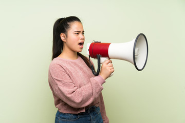 Wall Mural - Young teenager Asian girl over isolated green background shouting through a megaphone