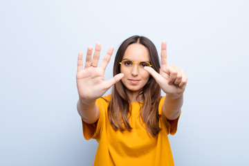 young pretty woman smiling and looking friendly, showing number seven or seventh with hand forward, counting down against blue wall