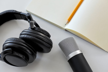 technology, sound recording and podcast concept - headphones , microphone and notebook with pencil on white background