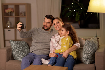 Sticker - people, family and technology concept - happy father, mother and little daughter taking selfie by smartphone at home at night