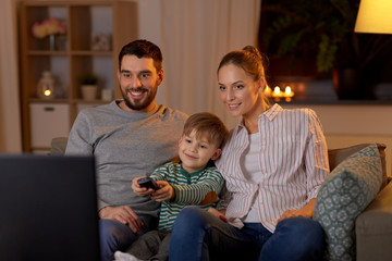 Poster - family, leisure and people concept - happy smiling father, mother and little son with remote control watching tv at home at night