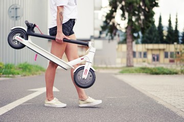 Young woman with modern electric scooter on blurry city street background.