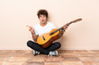 © luismolinero - Young caucasian man with a guitar sitting on the floor surprised and pointing side