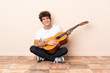 © luismolinero - Young caucasian man with a guitar sitting on the floor smiling a lot